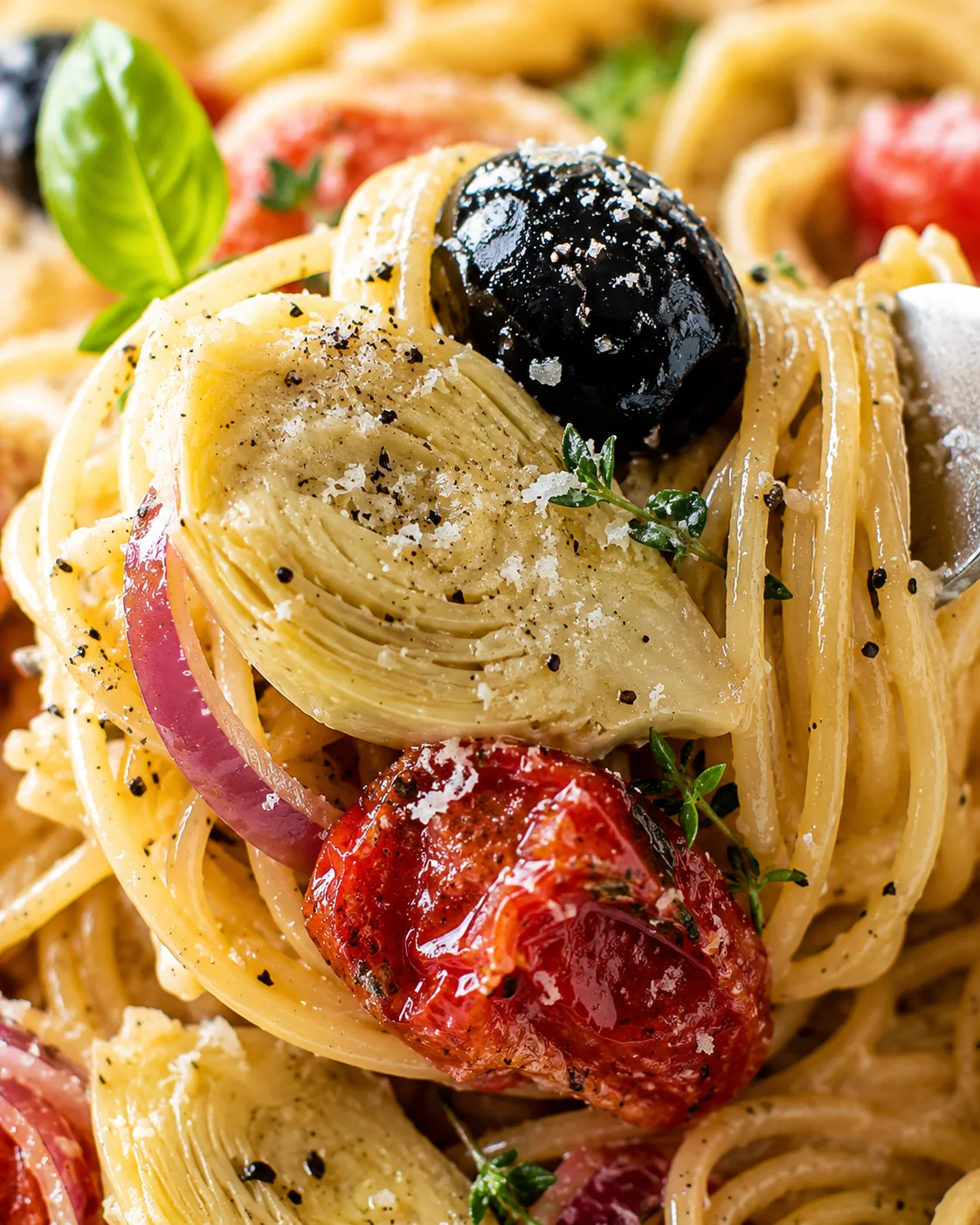 Close-up of colorful Mediterranean pasta with vegetables and herbs on top.