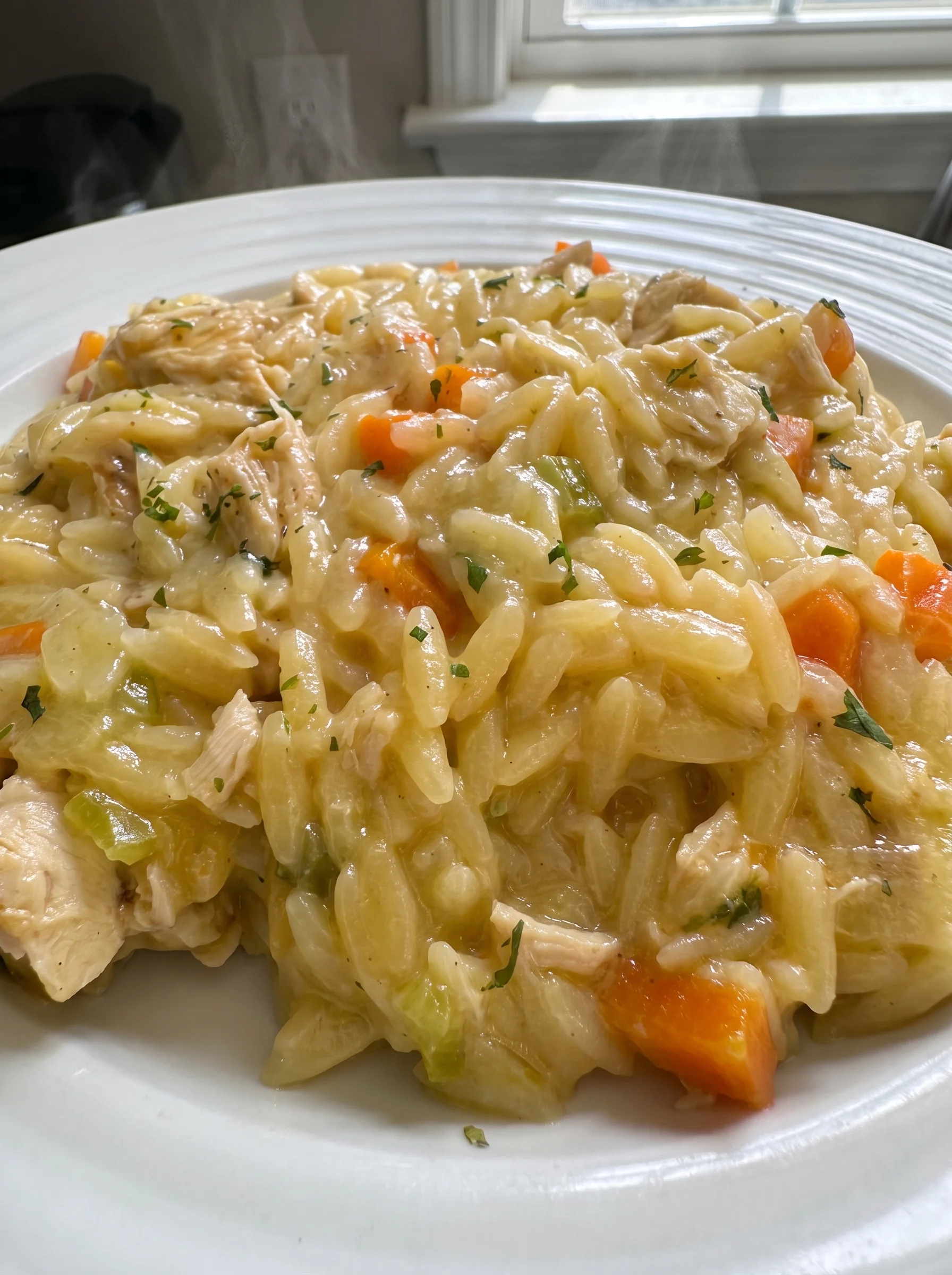 A close-up of a creamy chicken pot pie orzo dish on a white plate.
