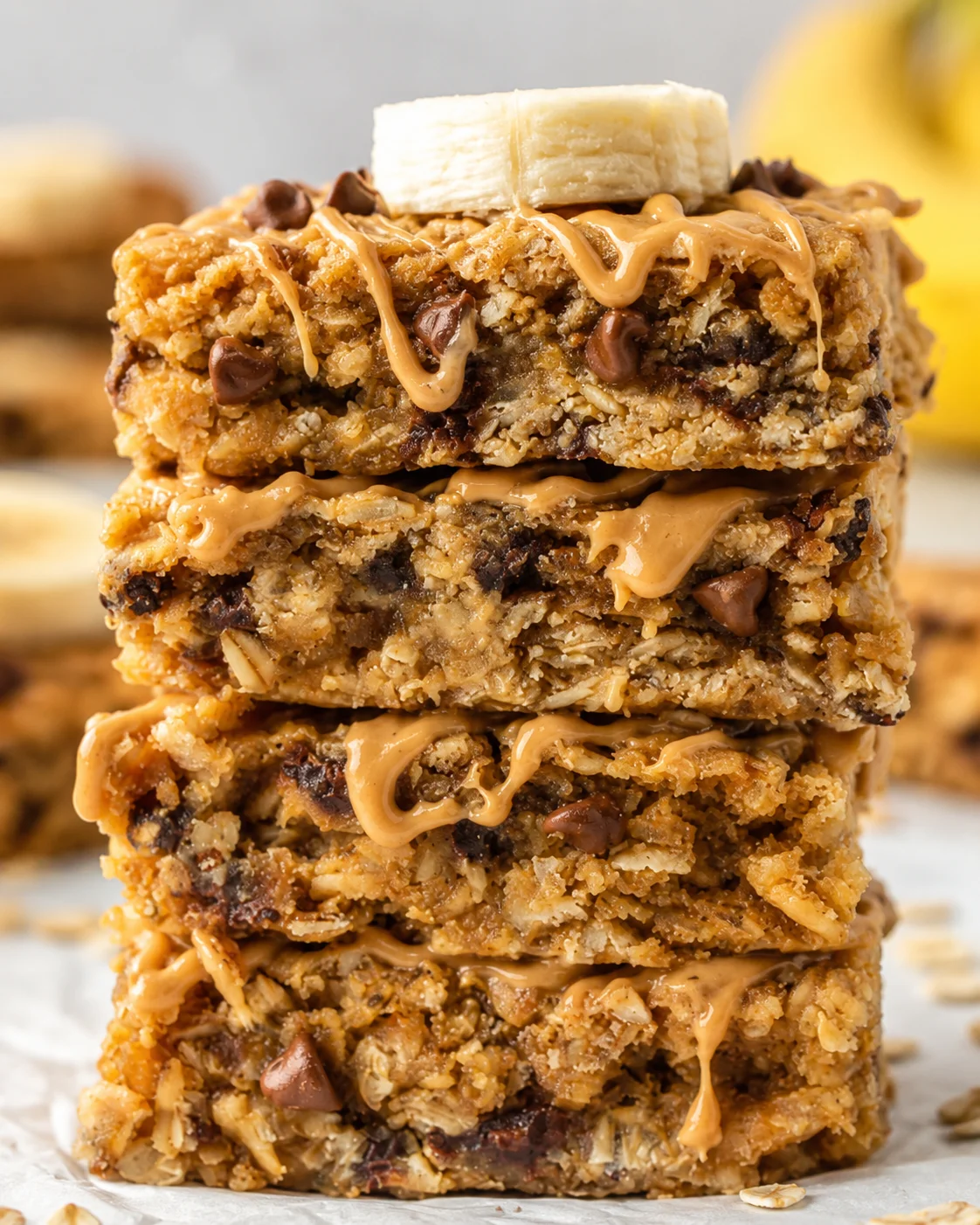 Stack of banana peanut butter oatmeal bars topped with banana slices and chocolate drizzle.