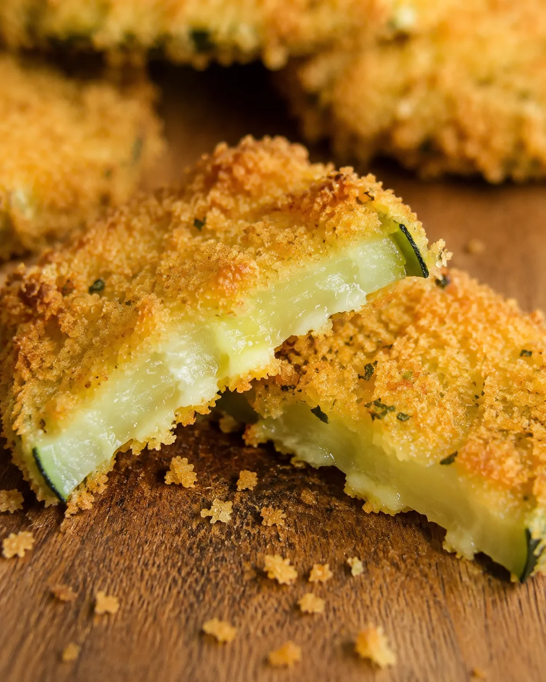 Golden, crispy zucchini chips with a breadcrumb coating served on a wooden surface