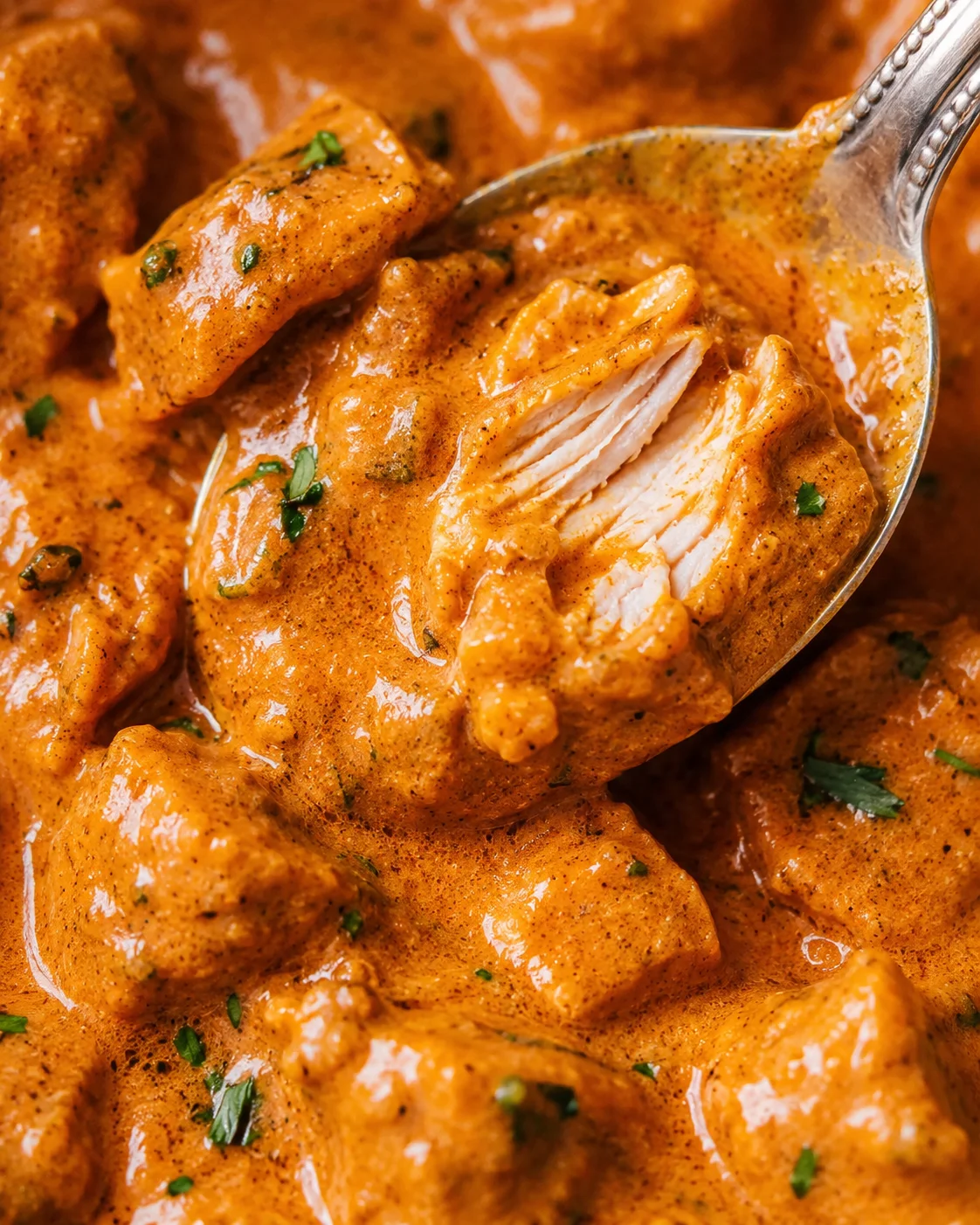 Tight view of a spoon revealing shredded chicken in creamy butter chicken sauce