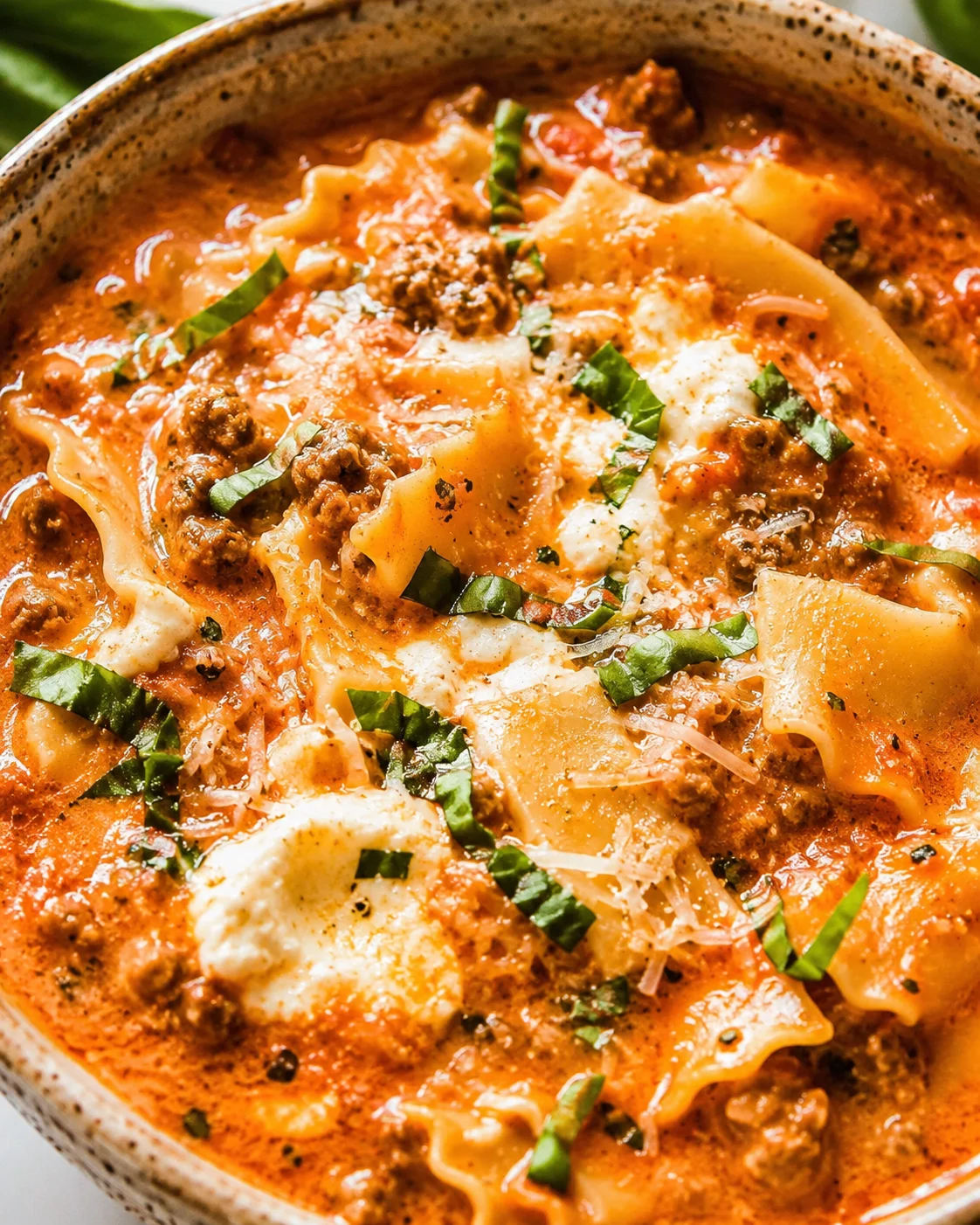 Close-up detail of Easy Creamy Lasagna Soup showing creamy broth, noodles, cheese and basil