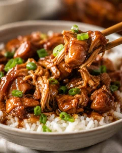 Crock Pot Bourbon Chicken served over white rice with green onions, a pair of chopsticks lifting a saucy bite
