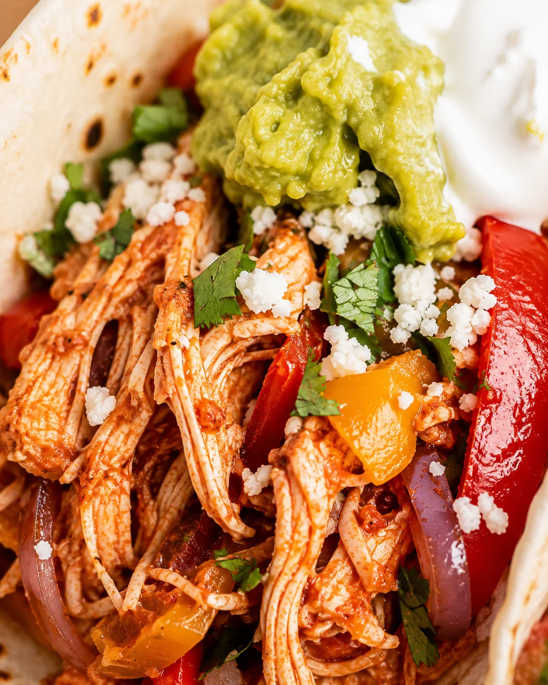 Close-up detail of shredded crock pot chicken fajita filling with bell peppers, guacamole, queso and cilantro