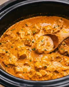 Slow cooker filled with creamy crockpot butter chicken and a wooden spoon