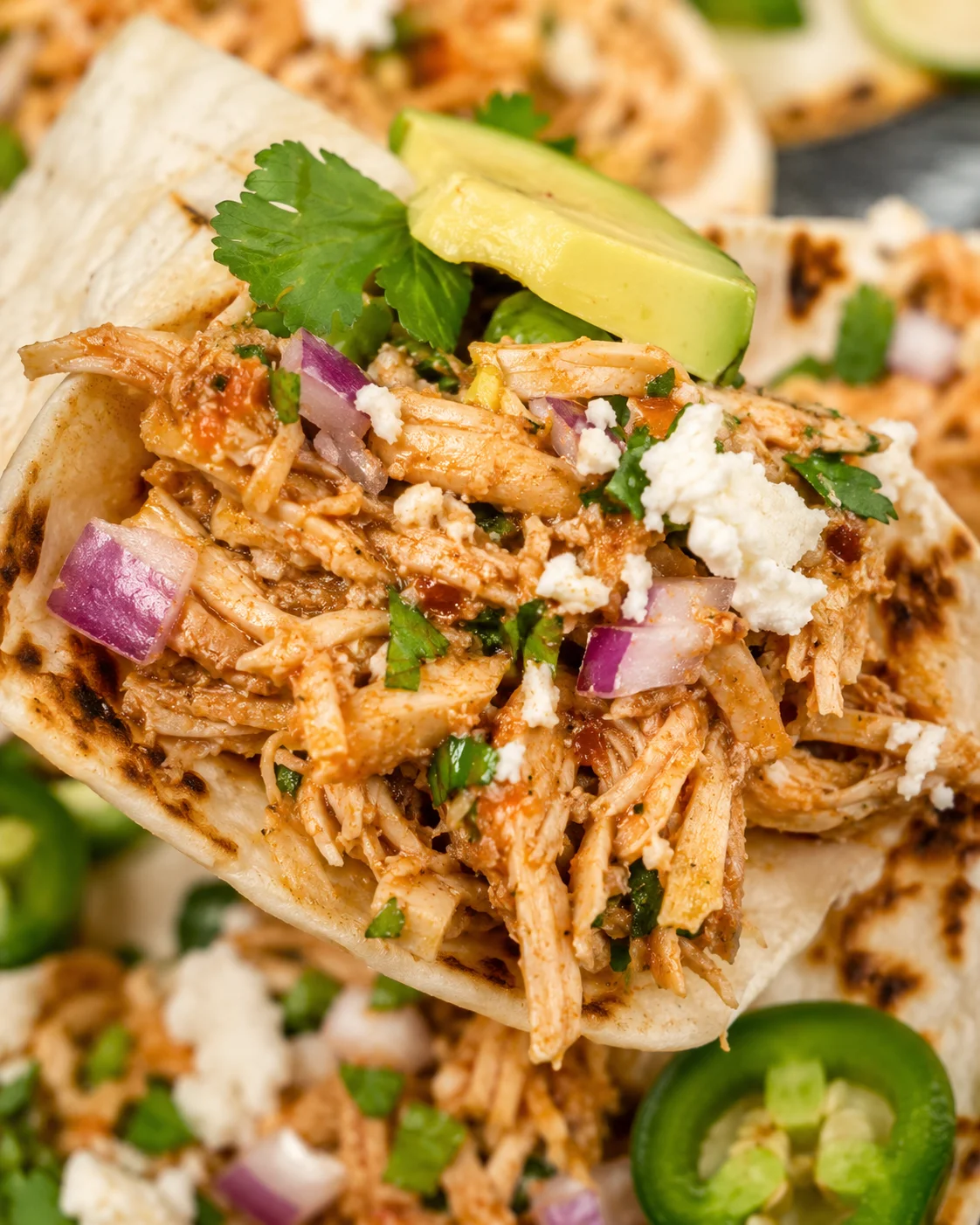 Close-up detail of shredded crockpot chicken taco filling with red onion, cilantro and crumbled cheese