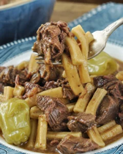 Crock Pot Mississippi beef noodles served on a blue plate with a pepperoncini and a forkful lifted